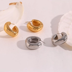 Close-up of thick C-shaped earrings with irregular metal texture in gold and silver