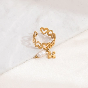 Close-up of gold heart-shaped hollow ring with pearl and cross charms on silk background