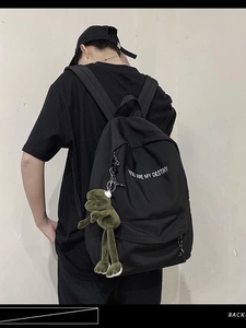Sac à dos d'étudiant noir avec texte blanc et breloque grenouille verte porté sur le dos