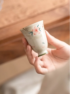 Close-up of hand-painted plum blossom ceramic tea cup with high foot and beige glaze