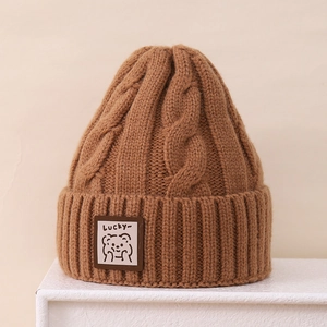 Detailed macro view of brown cable knit texture and embroidered bear patch on beanie