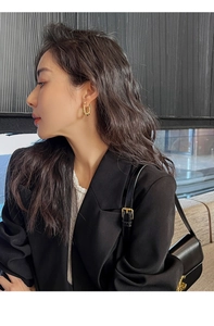 Close-up of model wearing vintage twisted gold hoop earrings with black blazer outfit