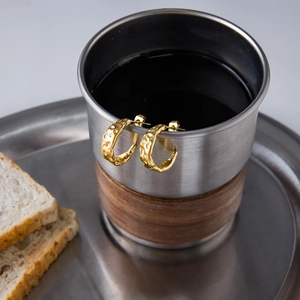 Gros plan de créoles dorées à texture martelée sur le rebord d'une tasse rustique