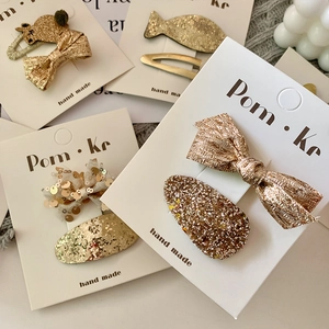 Sparkly gold sequin bow hair clip set for girls with handmade fabric details on a card