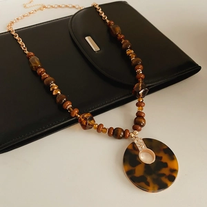 Gros plan d'un collier pendentif léopard avec perles de bois brun sur sac en cuir noir
