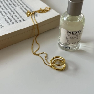 Detail of minimalist gold double ring pendant necklace on white surface with decor