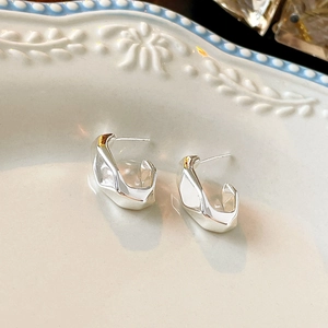 Detailed view of silver irregular C-shaped geometric earrings on a vintage white ceramic tray