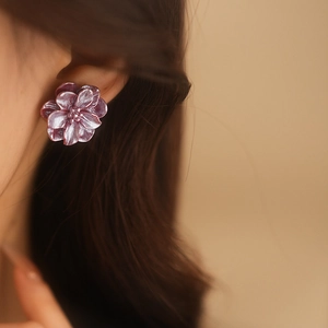 Gros plan sur d'élégantes boucles d'oreilles fleur en résine violette sur un modèle