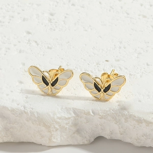 Detailed close-up of butterfly stud earrings with gold plating and black and white enamel