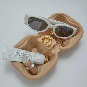 Flachbild eines goldenen Wickelrings auf Zellstoffschale mit Sonnenbrille und Armbanduhr