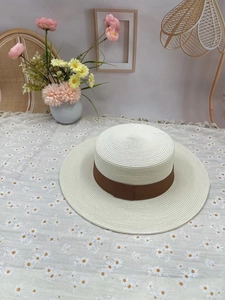 Detail of a beige woven boater hat featuring a wide coffee ribbon on floral background