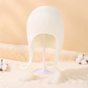 Close-up of white chunky knit baby hat with earflaps and braided tassel details