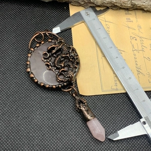 Macro shot of retro dragon pendant with pink crystal and calipers showing measurement