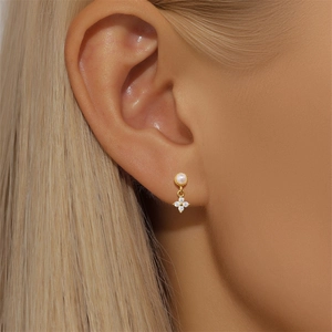 Close-up of elegant gold stud earring featuring a pearl and sparkling clover drop