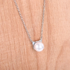 Detail view of the silver cat ear pendant with a round pearl on a wood surface