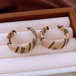 Close-up of beige fabric wrapped hoop earrings with letter print and golden metal stud