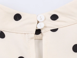 Détail de l'encolure à pois beige avec deux boutons blancs sur une robe en coton