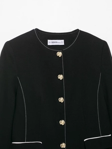 Detail of black tweed blazer featuring golden rose buttons and contrast white stitching