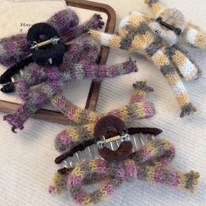 Three elegant knitted bow hair claws in purple, yellow, and pink stripes on wood