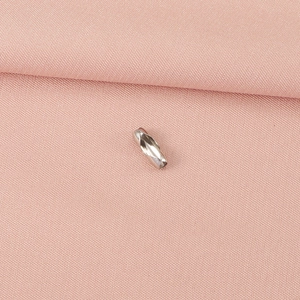 Détail macro d'un connecteur de chaîne à billes argenté sur tissu tissé rose