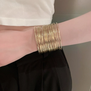 Detail of a wide gold multi-layer wire cuff bracelet worn on the arm in a minimalist style
