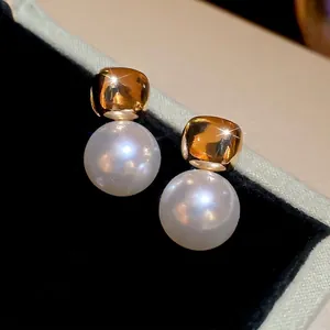 Elegant gold square stud earrings with large white round pearls on black velvet display