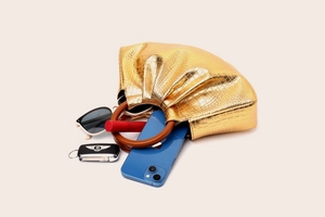 Golden pleated cloud bag with wooden handle showing interior capacity and small essentials