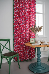 Detail of red floral cotton linen curtain with green tassel fringe in a retro room