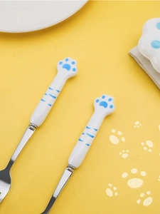 Close-up of cat paw ceramic handle spoon and fork set on a yellow patterned background