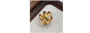 Macro detail of triple-layered gold ear cuff on textured linen and wood background