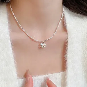 Collier en perles avec pendentif cheval à bascule porté sur un pull en peluche blanche