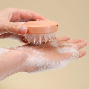 Brosse de massage cuir chevelu en silicone rose tenue en main avec mousse riche