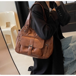 Brown vintage style tote bag shown on model with multiple buckle straps and flap pocket detail