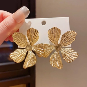 Detail of gold five-petal flower earrings with textured metallic finish on display