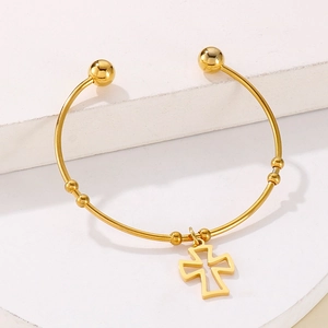 Detail of gold open bangle with hollow cross charm and beads on white stone background