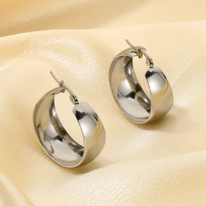Detailed close-up of silver wide hoop earrings on beige silk fabric with smooth finish