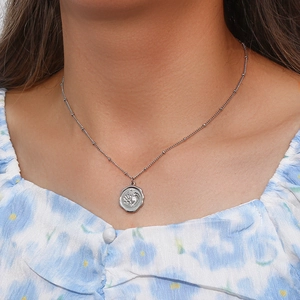Gros plan d'un collier argenté avec pendentif empreinte de bébé porté sur la peau