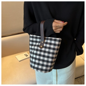 Detail of checkered canvas bucket bag featuring brown leather handles and rivets
