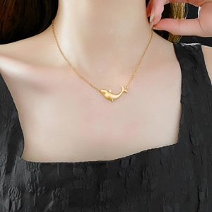 Close-up of a gold whale pendant necklace with zircon stones worn by a model