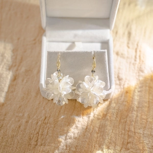 Macro detail of white shell flower earrings with gold tassels on jewelry display