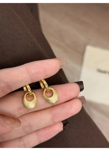 Makroaufnahme goldener ovaler Metallohrringe mit mattierter Textur und klassischem Haken