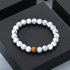Macro view of white turquoise beads with a central brown tiger eye stone on a black stand