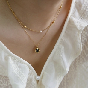 Detail of 18K gold layered necklace with white pearl and oval black gemstone pendant