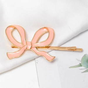 Elegant gold metal hair clip featuring a pink enamel bow on a soft white silk texture