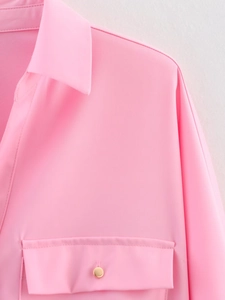 Close-up of pink safari style shirt featuring a classic collar and gold button chest pocket
