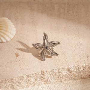 Macro shot of silver starfish ear clip with fine texture on a natural sandy beach surface