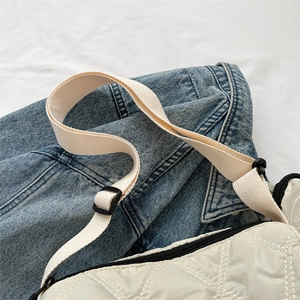 Sac bandoulière matelassé beige avec surpiqûres losanges sur une veste en jean