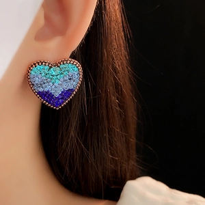 Macro shot of heart-shaped earrings with blue gradient crystals on a rose gold base