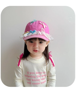 Detail of pink children's sun hat featuring white lace, ribbon bows, and pearl accents