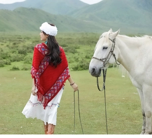 Outdoor shot of a red ethnic knit shawl with blue geometric patterns and fringe detail